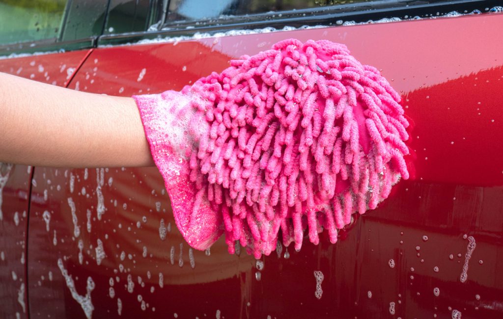Female hand holding pink mitt with bubbles for washing car.