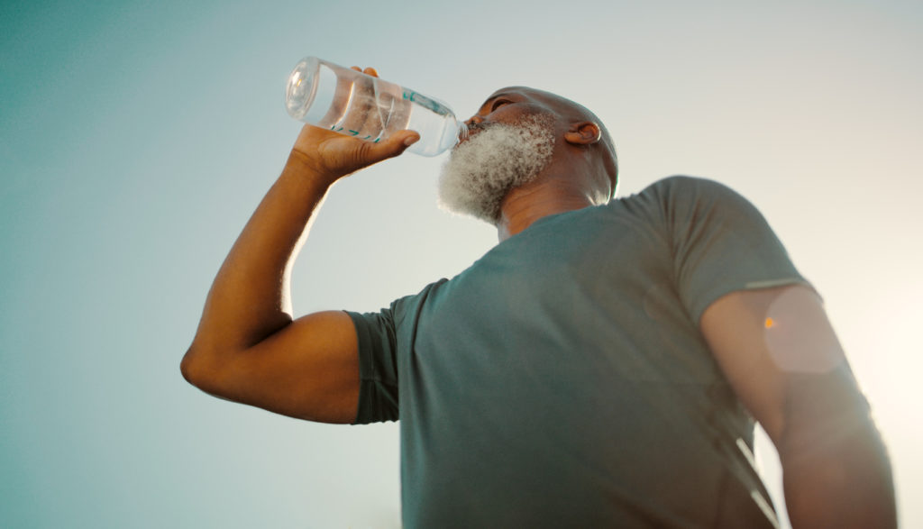 Low angle shot of a senior man standing alone and drinking water after a workout in his back garden
