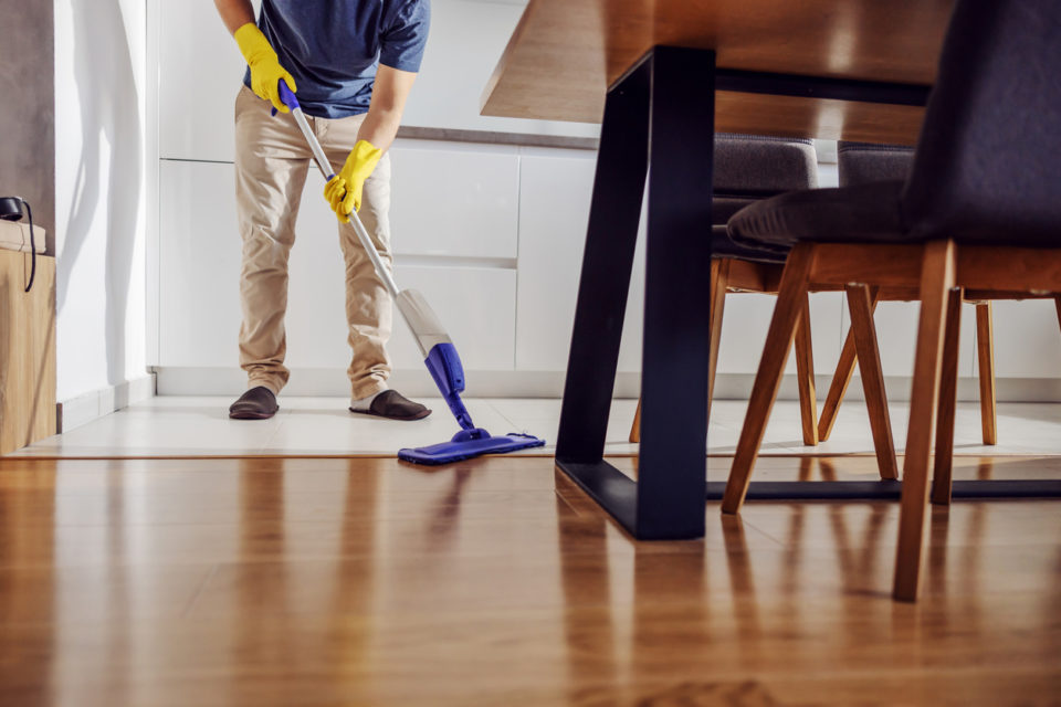 Cropped picture of tidy young man with rubber gloves cleaning kitchen floor with mop.