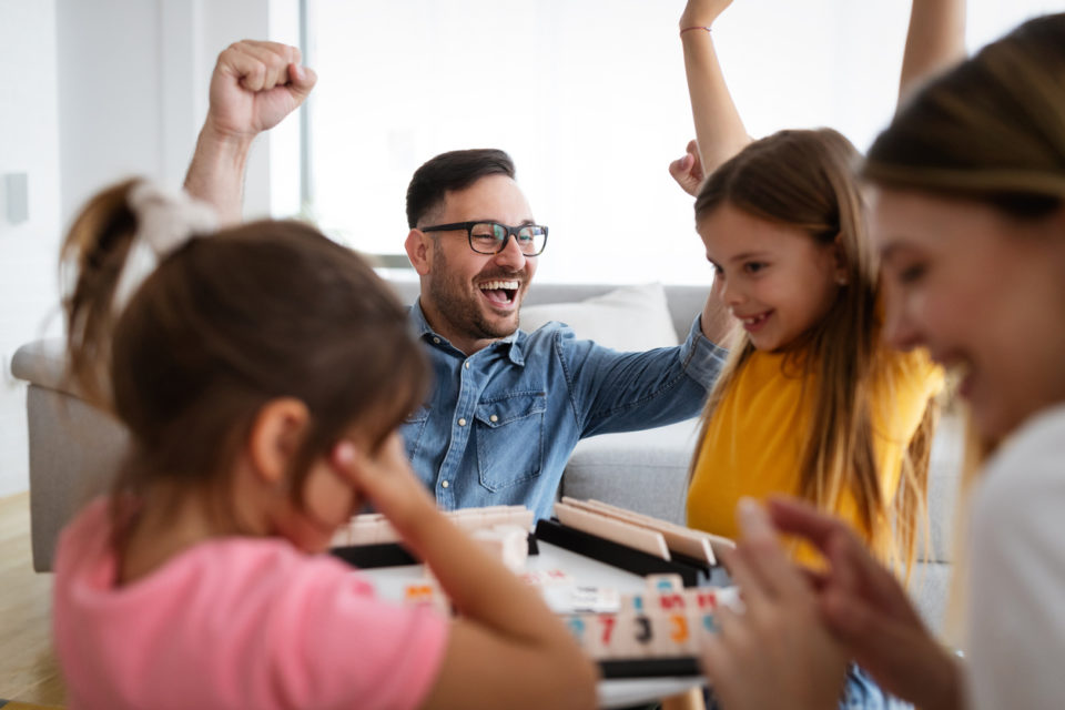 Happy parents and children having fun, playing board game at home