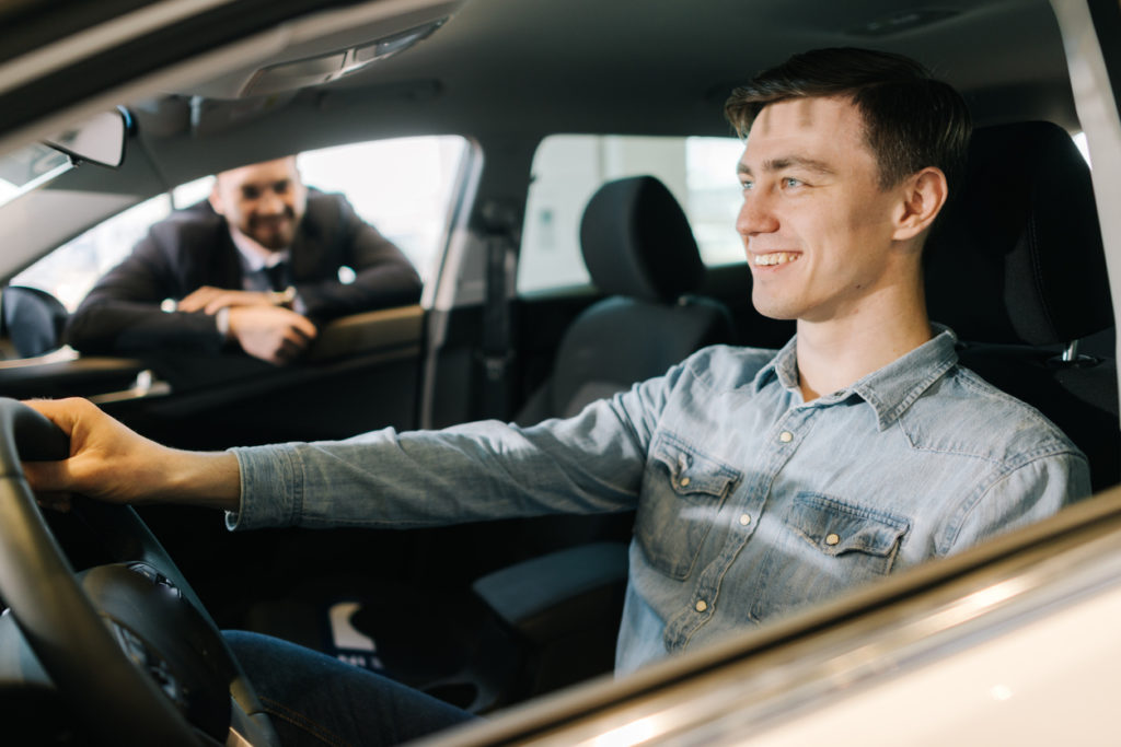 Happy young man behind the wheel of new car in auto dealership.