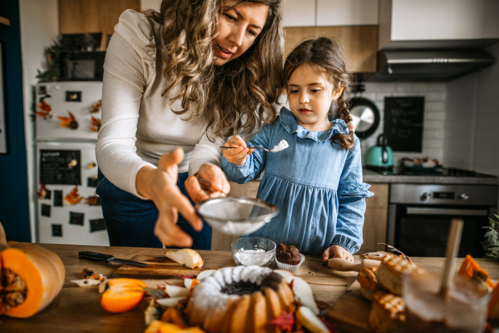 Mother and her little cute daughter are dusting cake