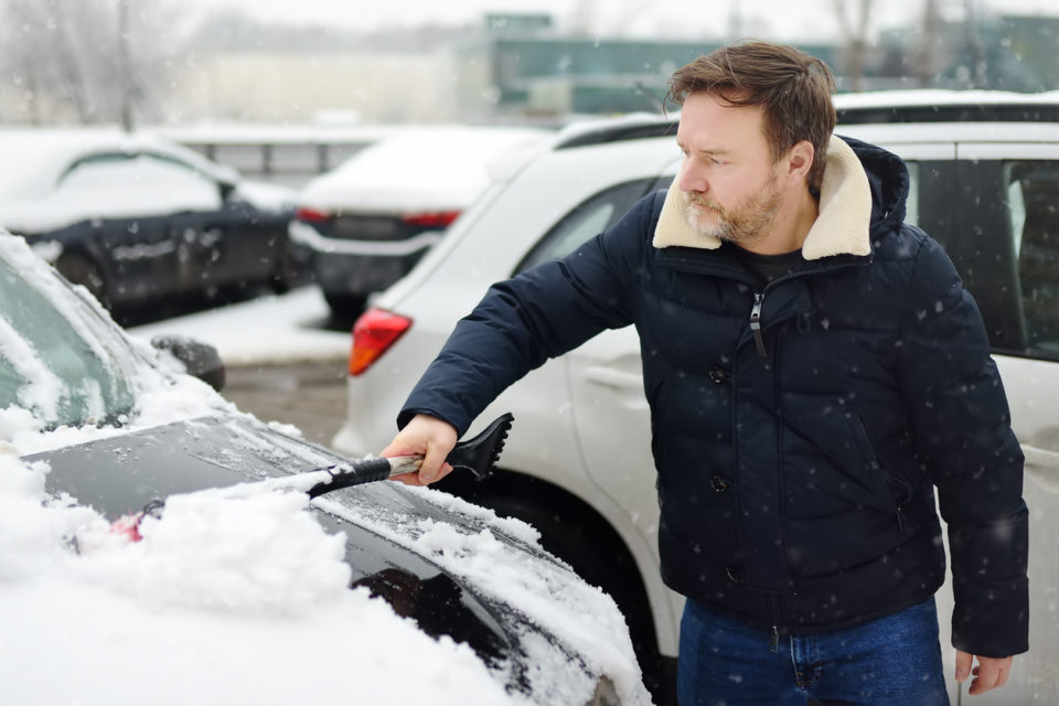 A mature man cleans his car with a brush after a snowfall.