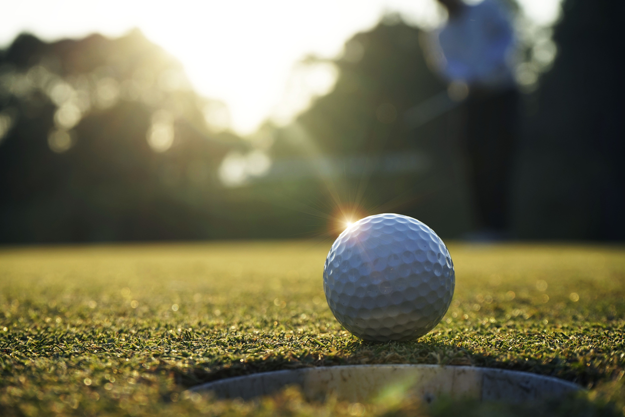 Golf ball putting on green grass near hole golf to win in game at golf course with sunset background